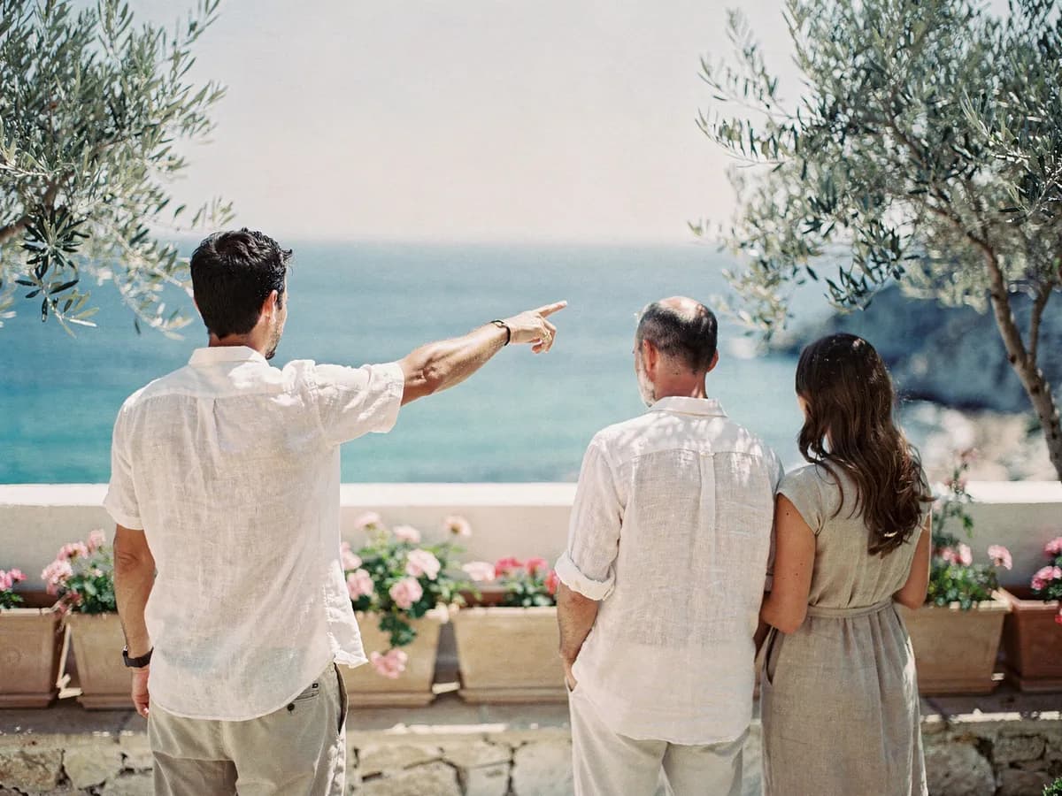 A host pointing out across the sea from a garden terrace beside a couple